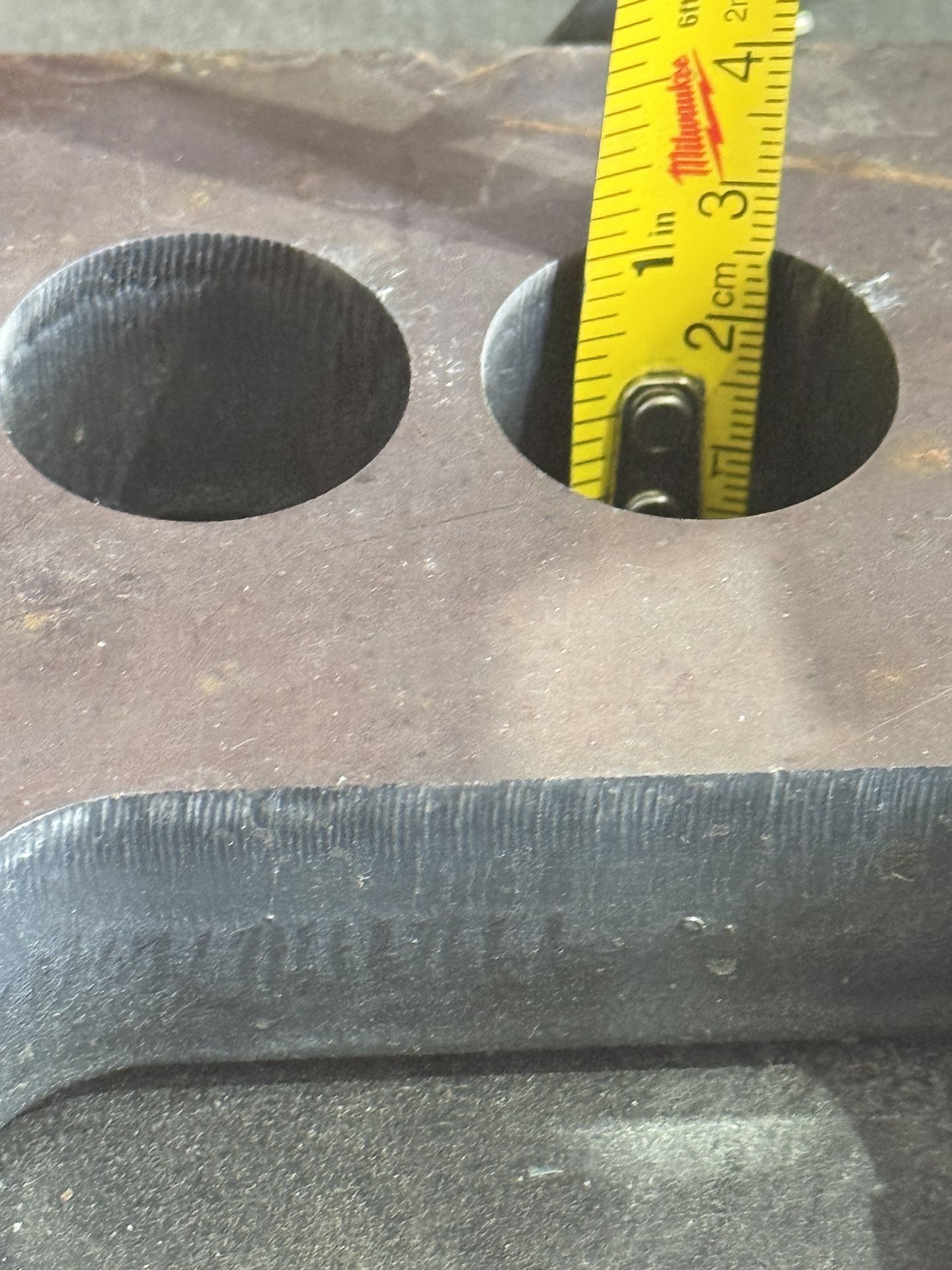 Thick steel plate with holes and a tape measure showing scale